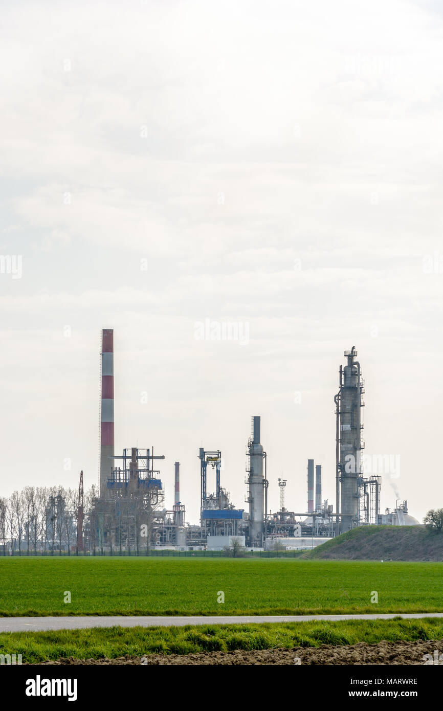 View of an oil refinery with smokestacks surrounded by crop fields in the french countryside under a pale sunlight. Stock Photo