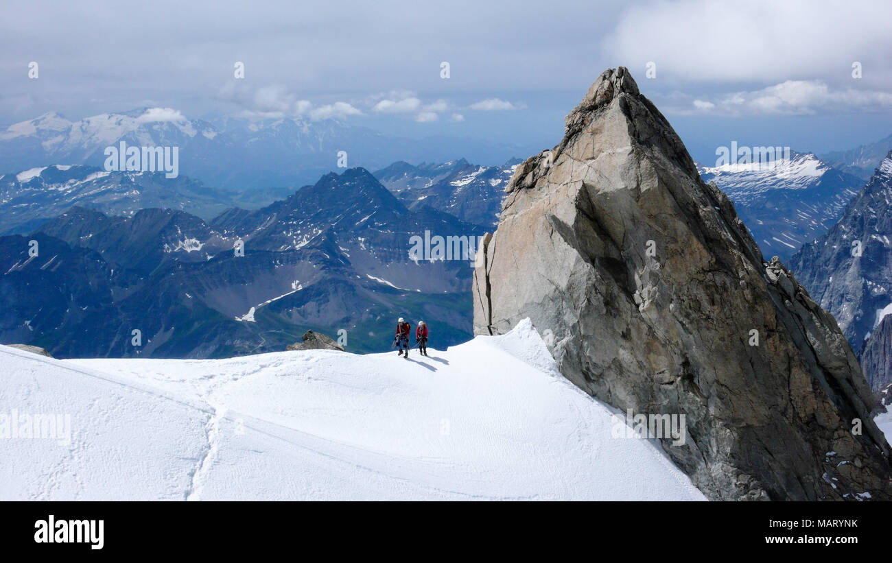 mountain guide and client walk along a narrow snow ridge with a giant ...