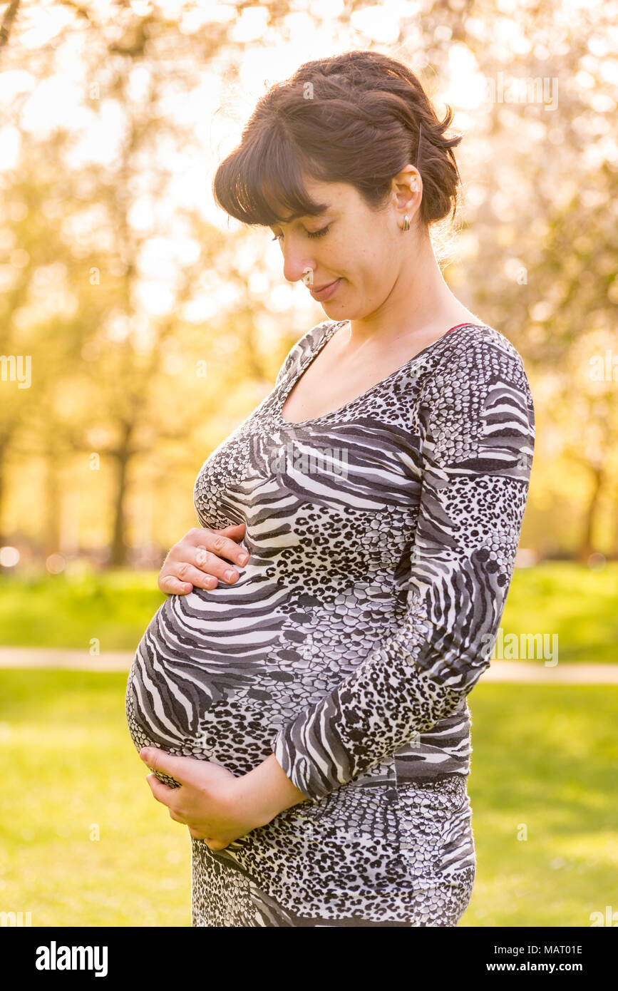 Pregnant woman in a park holding her belly, UK Stock Photo - Alamy