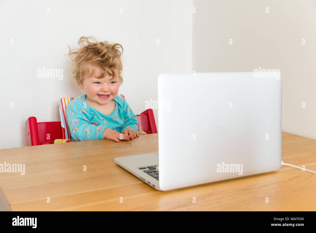 One year baby girl watching screen of laptop computer, England, UK Stock Photo