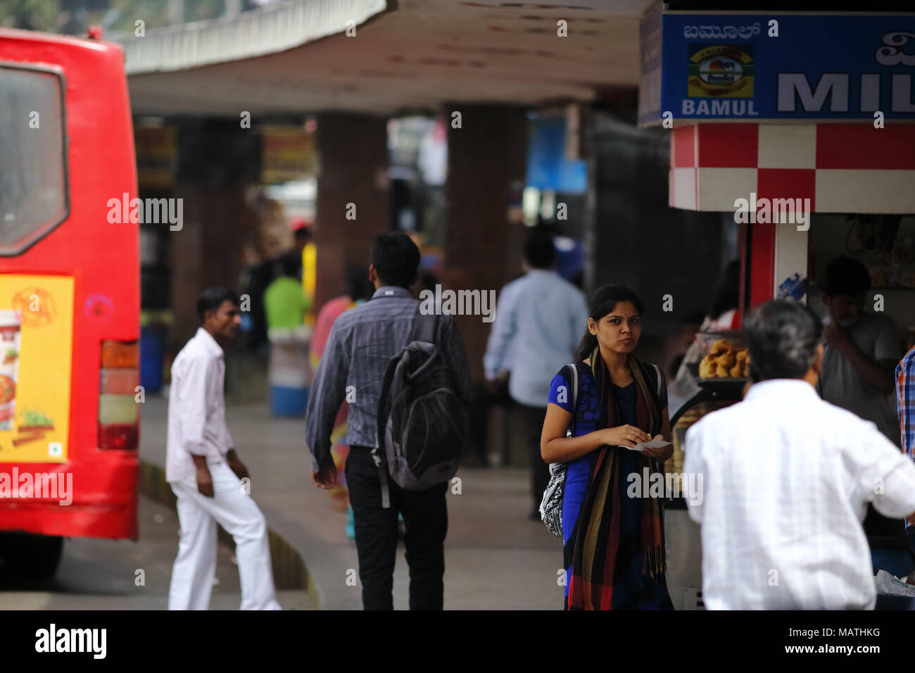 Bangalore, India - October 23, 2016: Unknown Indian girl in traditional wear stands eating samosa in the city bus terminal, a delicious local food. Stock Photo