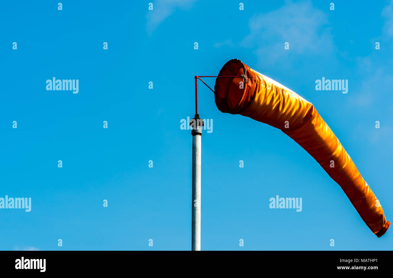 Orange windsock in moderate wind on white pole against clear blue sky on sunny day at aviation area. Wind direction sign at the airport field Stock Photo
