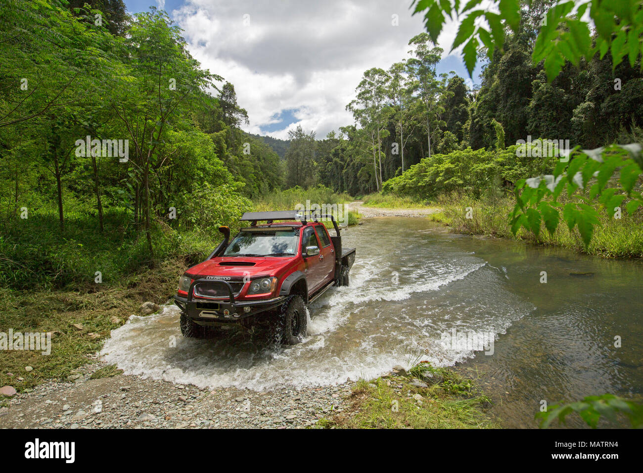 Red four wheel drive vehicle crossing creek hemmed with emerald forests in Conondale Ranges National Park Queensland Australia Stock Photo