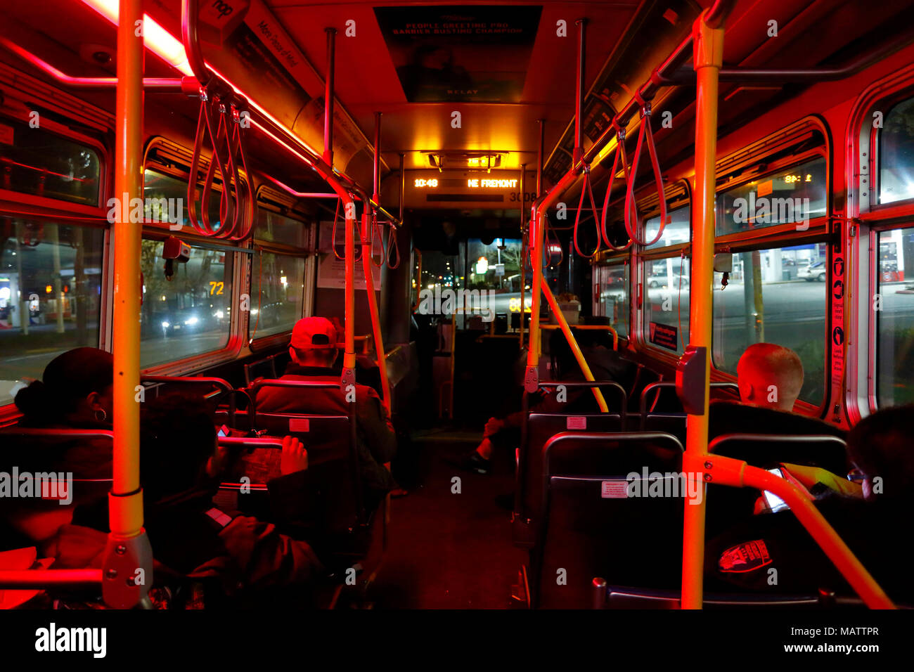 People riding a Portland, Oregon TriMet bus at night. The bus is dimly lit red inside to increase visibility, and safety for the bus driver Stock Photo