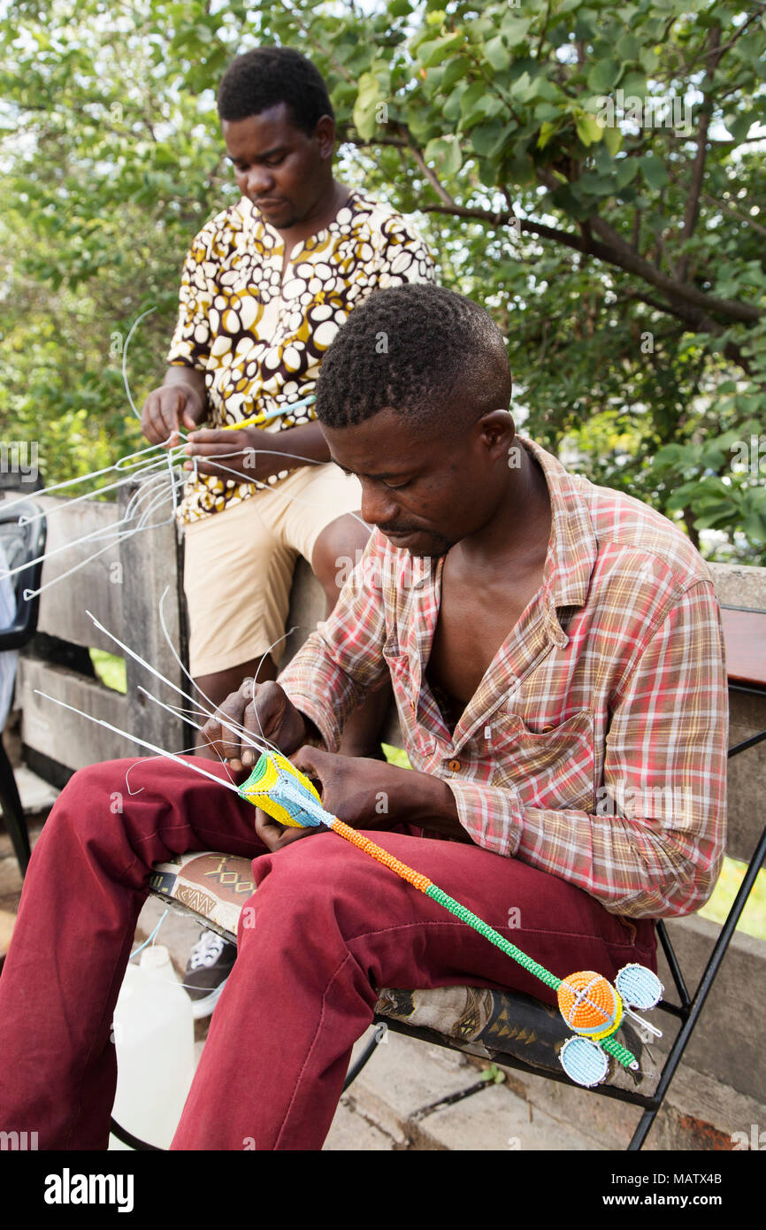 Men craft beadwork souvenirs in Harare, Zimbabwe. The men ply their