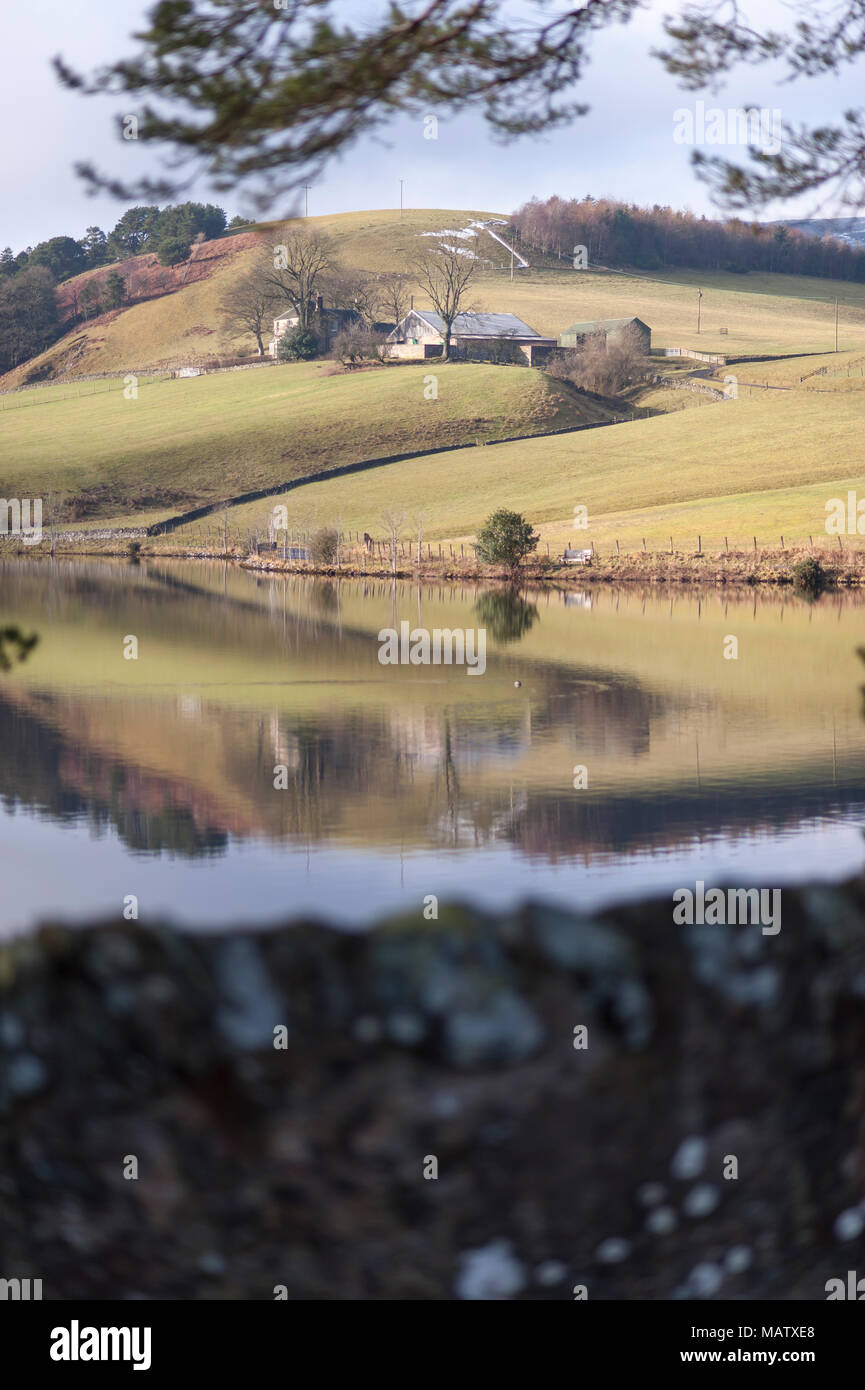 A farm on a hill is reflected in the water of a lake Stock Photo