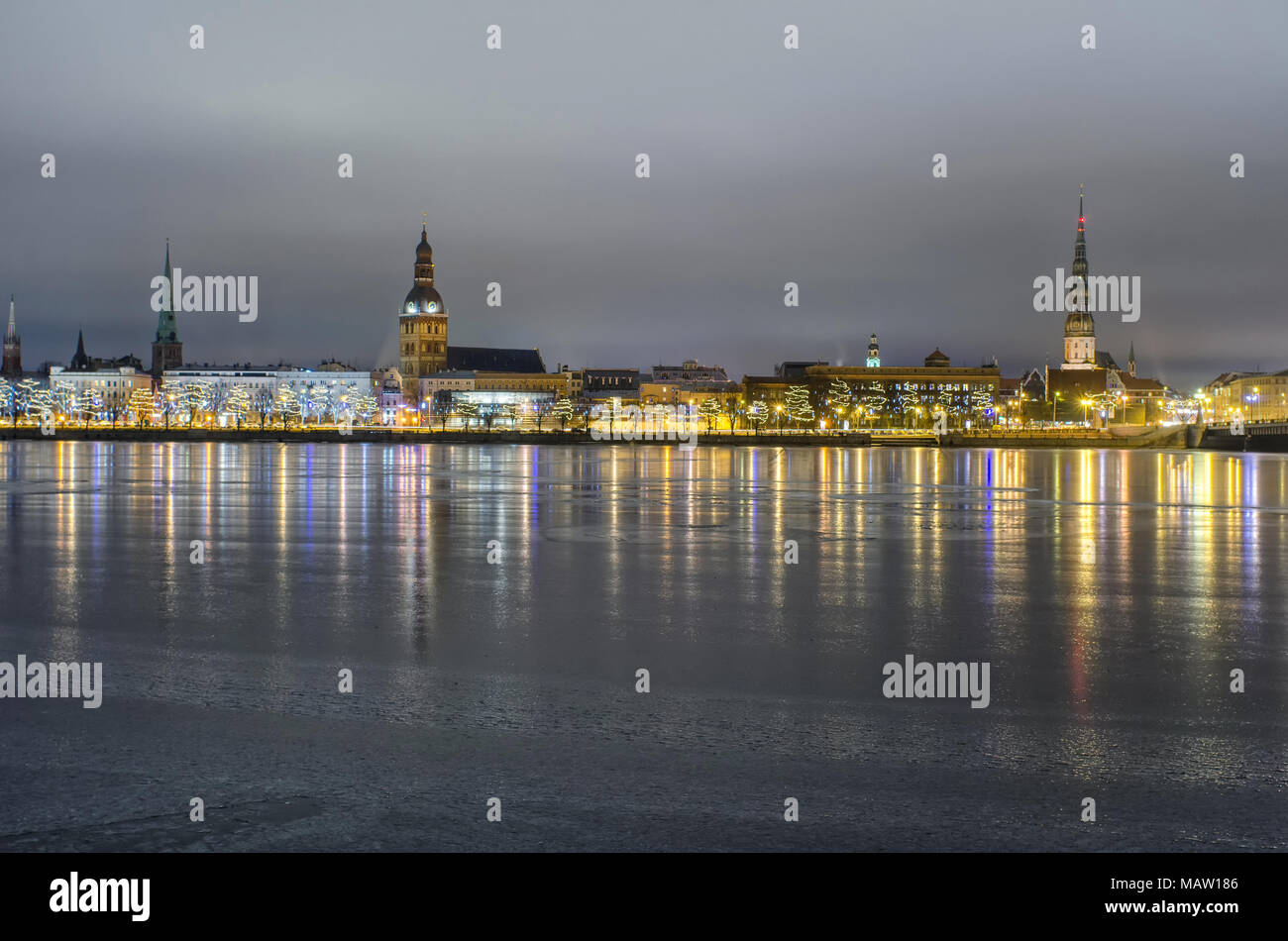 View of the old city of Riga with its bright lights  in Latvia over the frozen river Daugava at night in winter Stock Photo