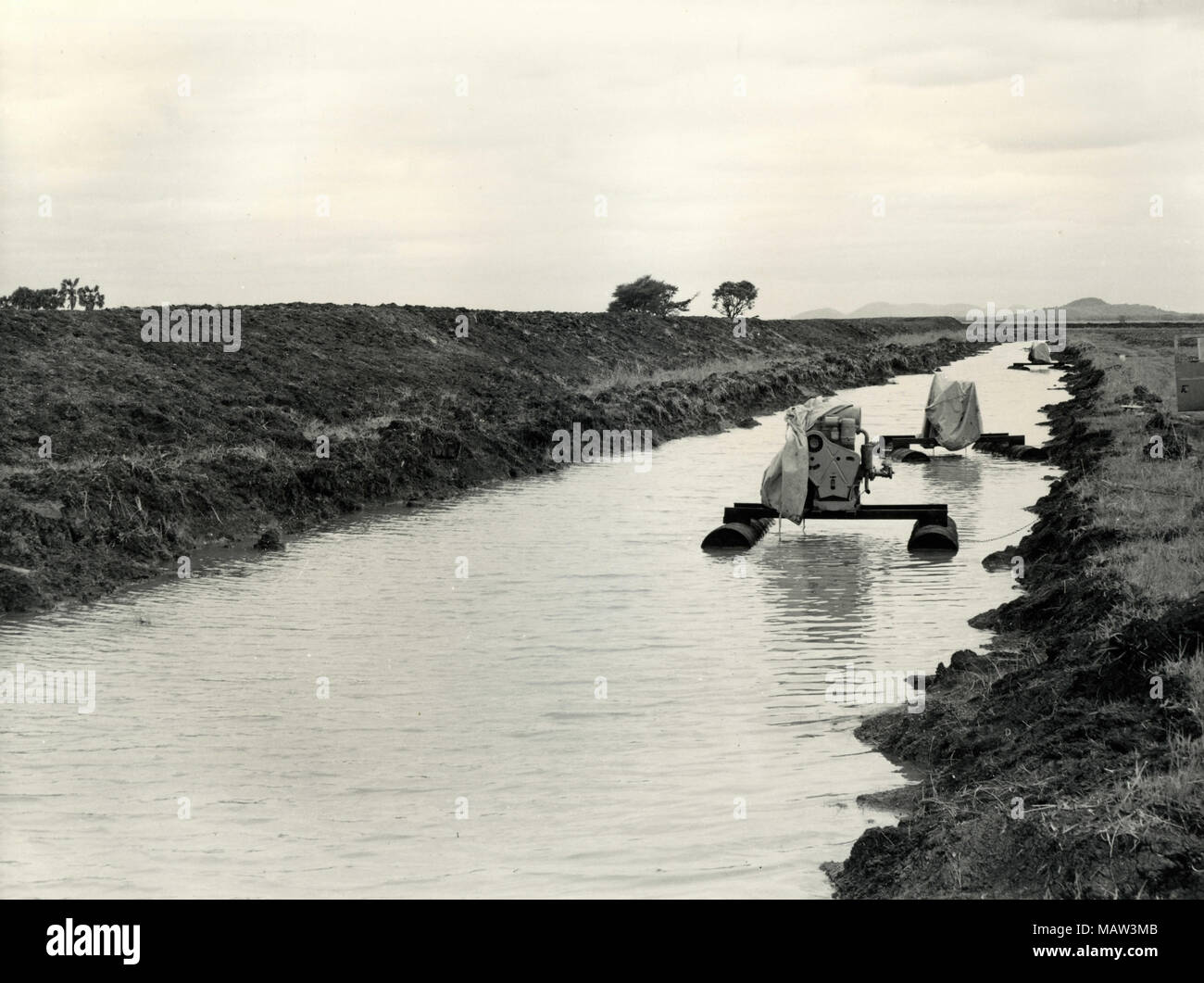 Irrigation canal adjacent to river bank dyke with floating irrigation pump, Rhodesian Selection Trust, Kafue Pilot Polder, Zambia, South Rhodesia 1957 Stock Photo
