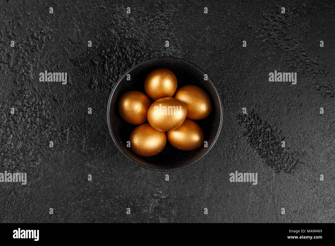 Golden eggs in a black cup on a black textured background. Easter eggs. Stock Photo