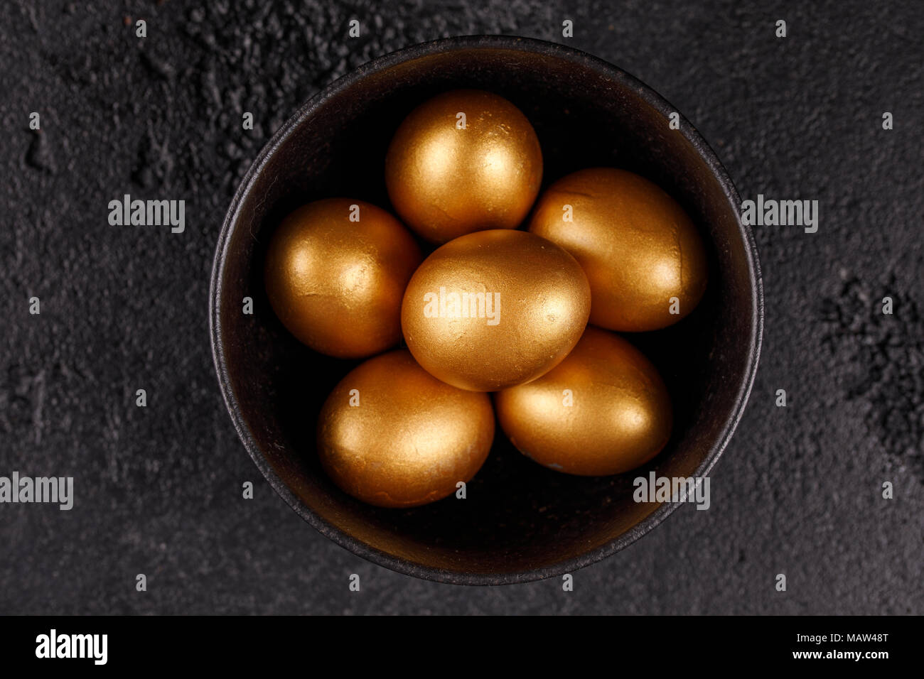 Golden eggs in a black cup on a black textured background. Easter eggs. Stock Photo