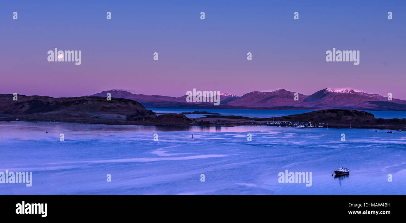 The Full Moon setting over the western islands of Scotland as the sun rises on Easter Sunday 1 April 2018. Viewed from McCaig's Tower in Oban Stock Photo