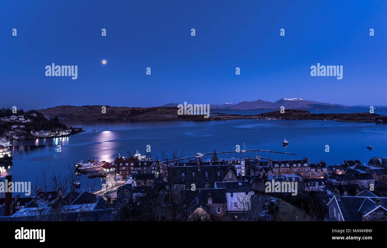 The Full Moon setting over the western islands of Scotland as the sun rises on Easter Sunday 1 April 2018. Viewed from McCaig's Tower in Oban Stock Photo