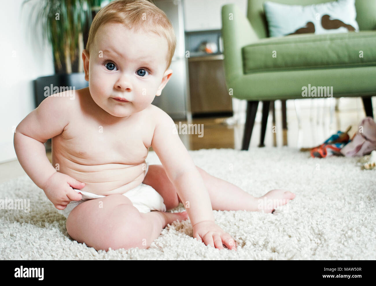 A six month old baby sitting up in a living room. Stock Photo