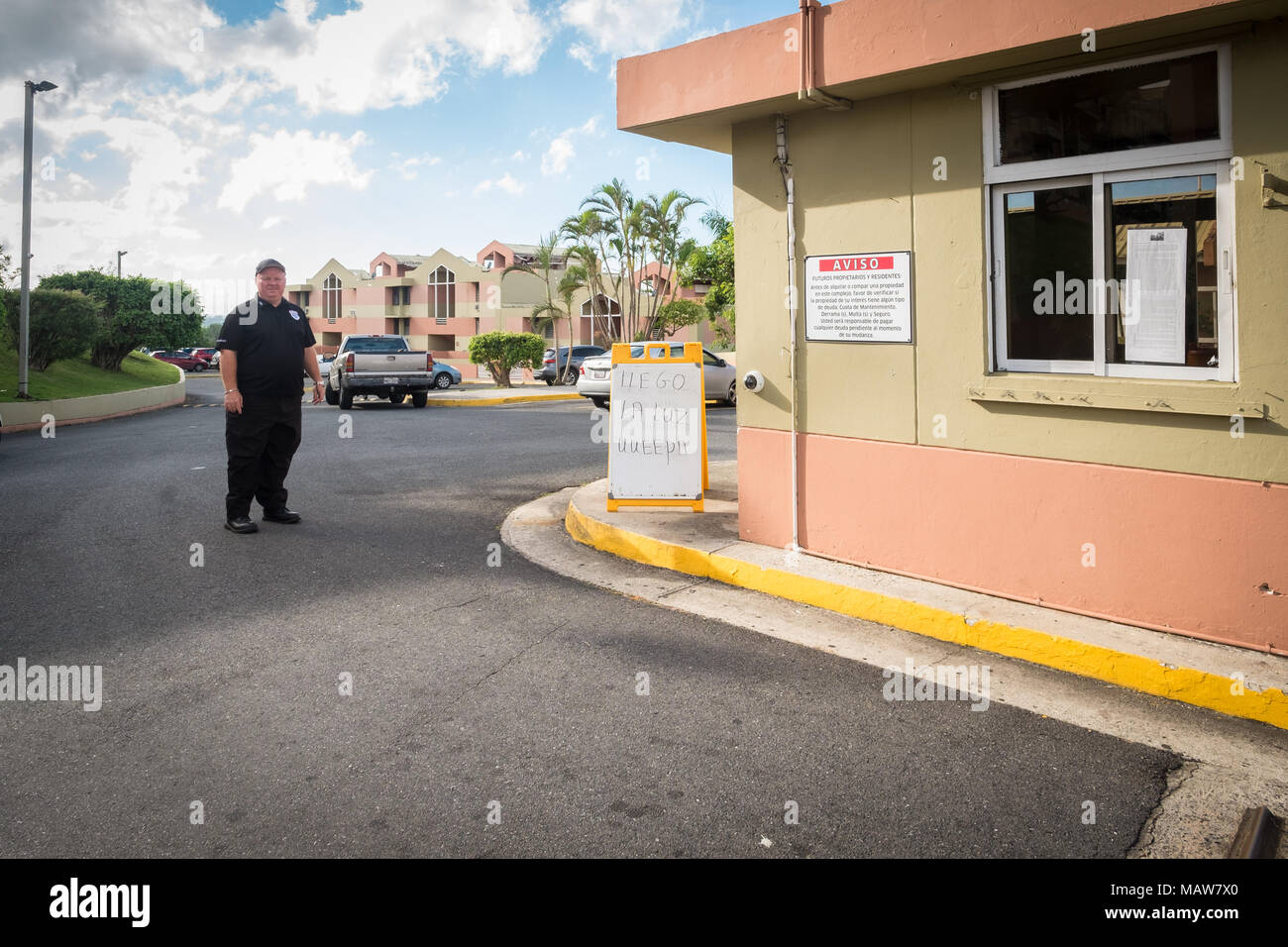 Caimito, Puerto Rico. 30th November, 2017. A security guard of a condominium complex stands proudly next to a sign announcing the recent restoration of power to the building several months after Hurricane Maria devestated the isaldn of Puerto Rico. Credit: Sara Armas/Alamy Reportage. Stock Photo