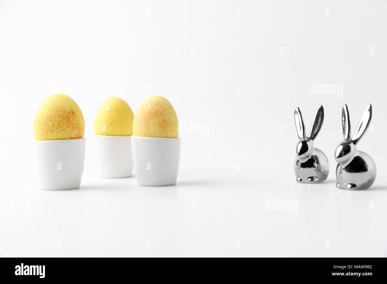 yellow painted easter eggs in egg stands and statuettes of rabbits on white Stock Photo