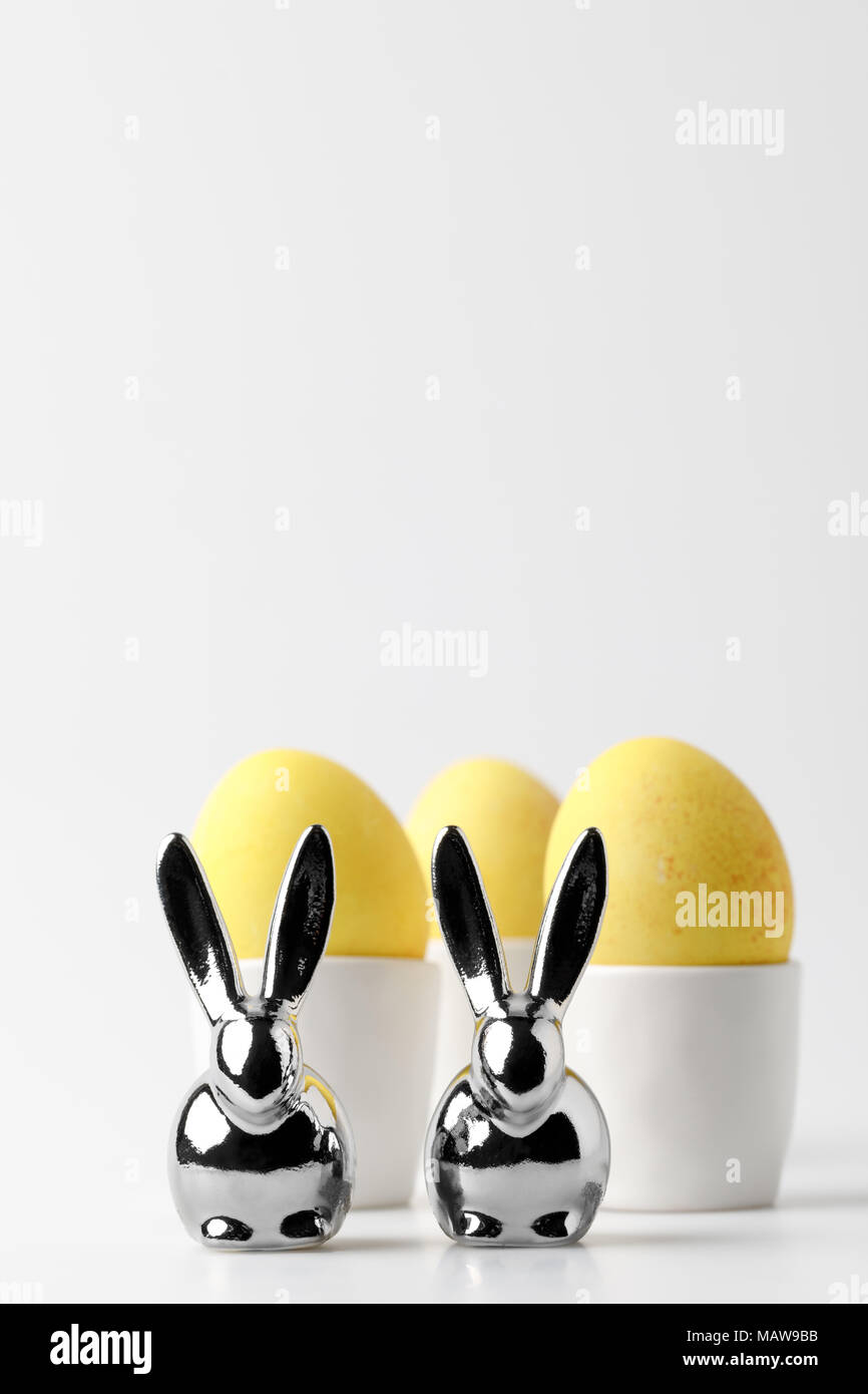 yellow painted easter eggs in egg stands and statuettes of rabbits on white Stock Photo
