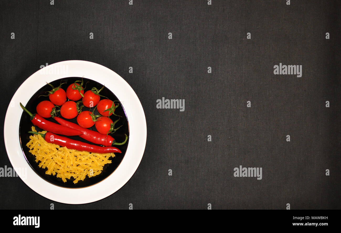 White and black plates with tomatoes, hot chili peppers and pasta, copy space, minimalist style, top view Stock Photo