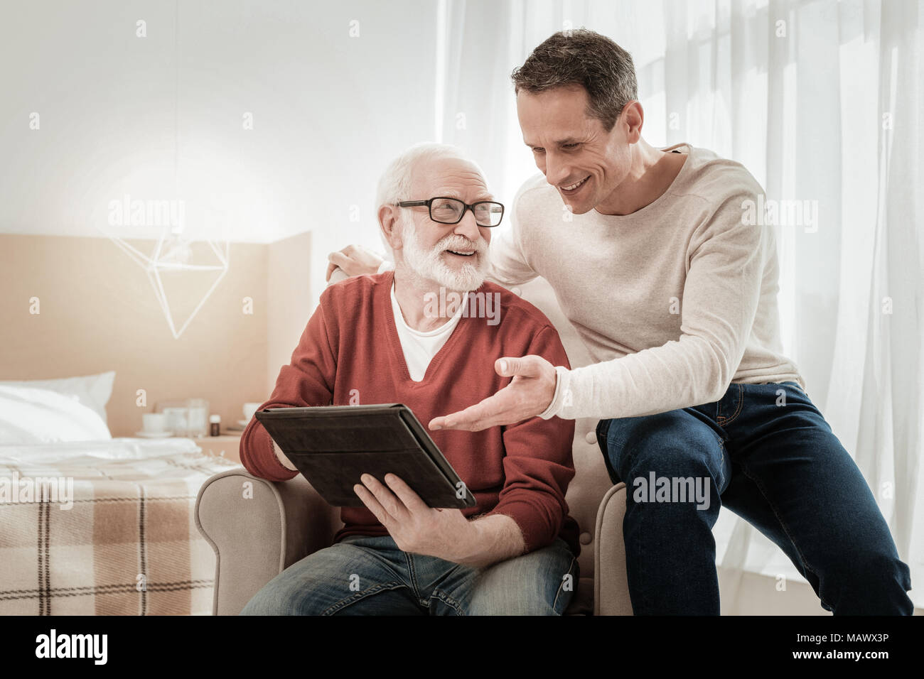 Funny pleasant men sitting and overlooking the tablet. Stock Photo
