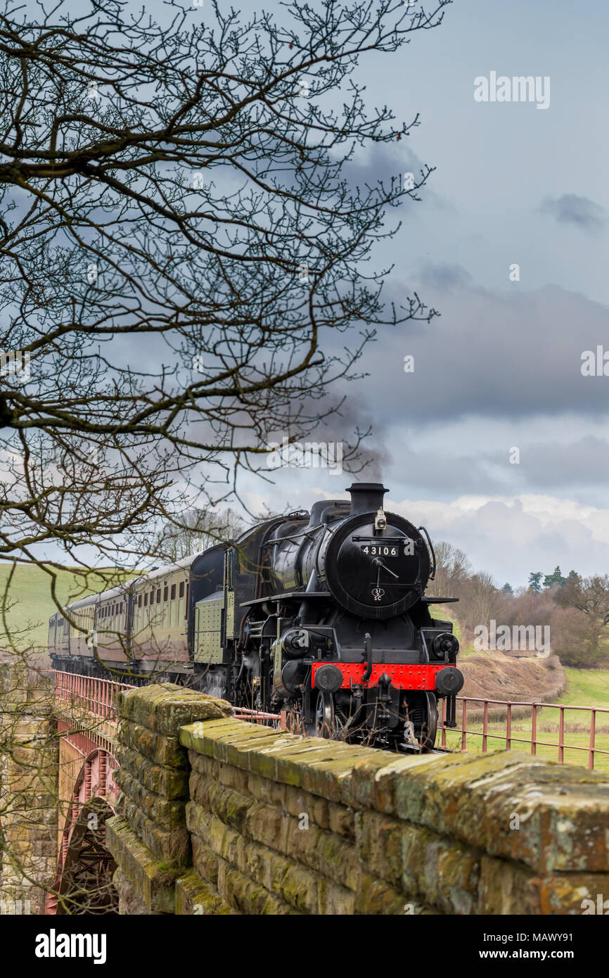 Front view of old, vintage UK steam locomotive 43106 approaching, puffing smoke, travelling through scenic English countryside in spring. Stock Photo