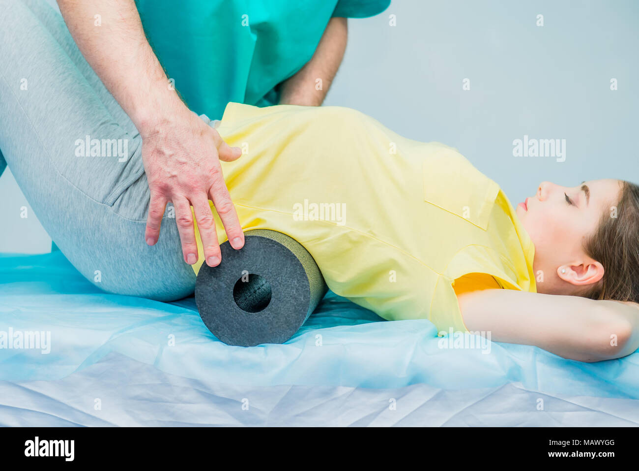 Woman at the physiotherapy doing physical exercises with her therapist, they using a massage roll. A chiropractor treats patient's loins spine in medi Stock Photo