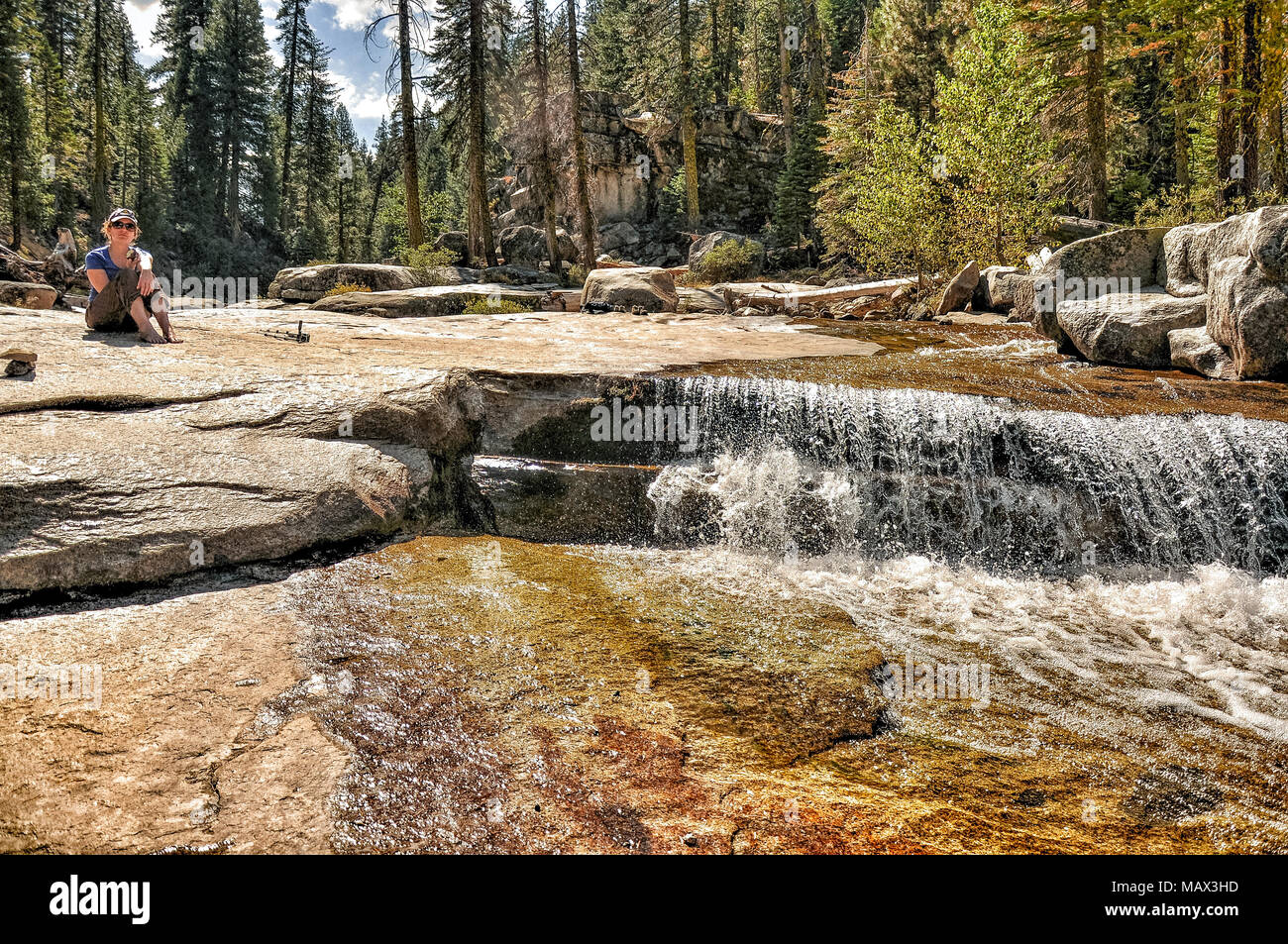 Woman sitting near stepped falls in wilderness on sunny day, John Muir Wilderness, California, USA Stock Photo