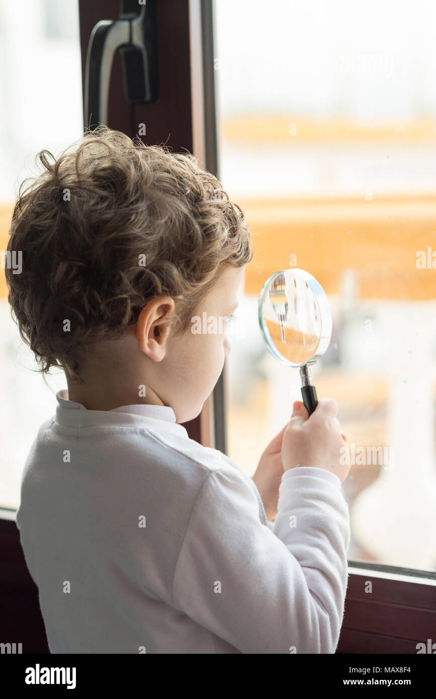 Child looking through a big window through a magnifying glass Stock Photo