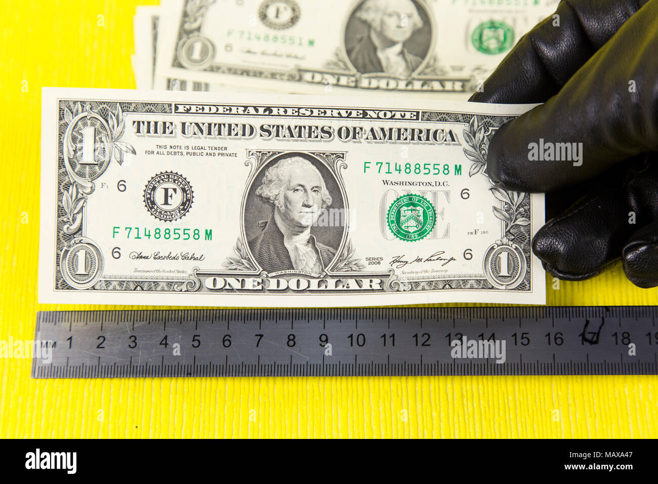 Counterfeiters measure counterfeit money bills with a ruler on a yellow background Stock Photo