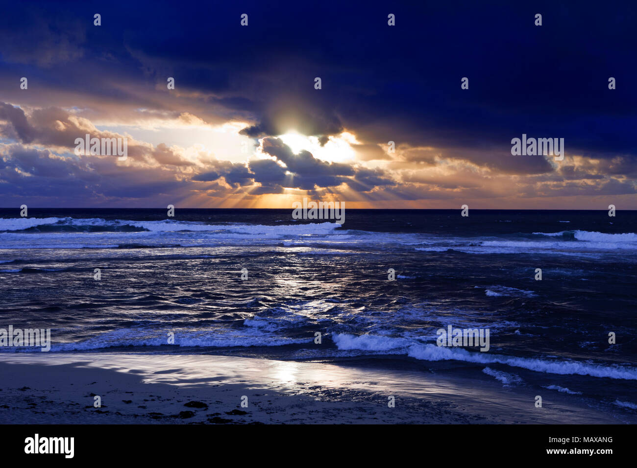 Sea scape with waves and dramatic dark clouds with a shaft  of sun rays during sunset Stock Photo