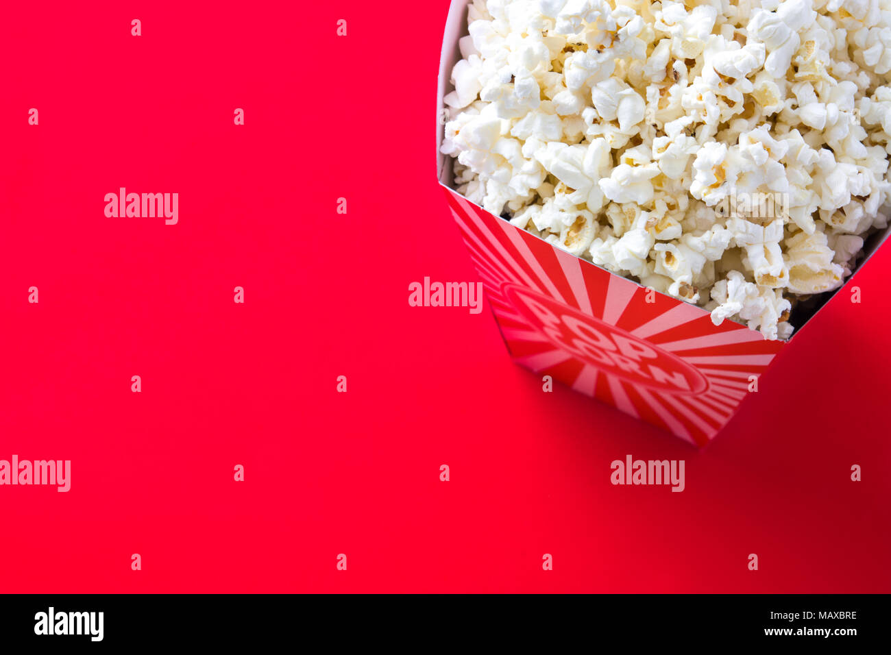 Striped box with popcorn on red background. Copyspace Stock Photo