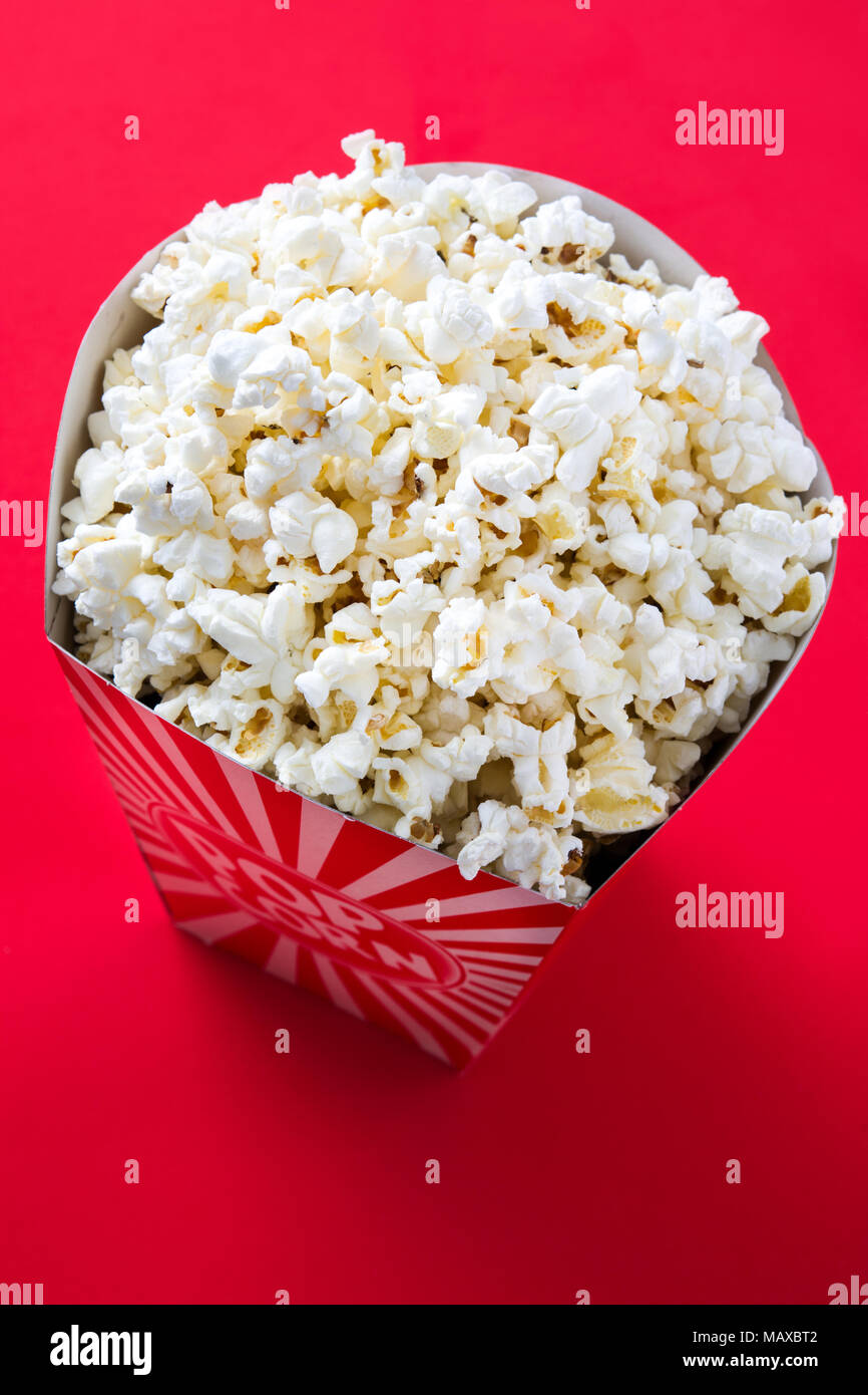 Striped box with popcorn on red background. Stock Photo