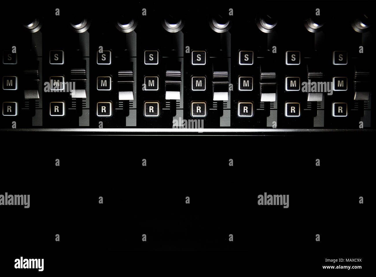 Audio studio mixer volume level sliders and dials edge lit on black