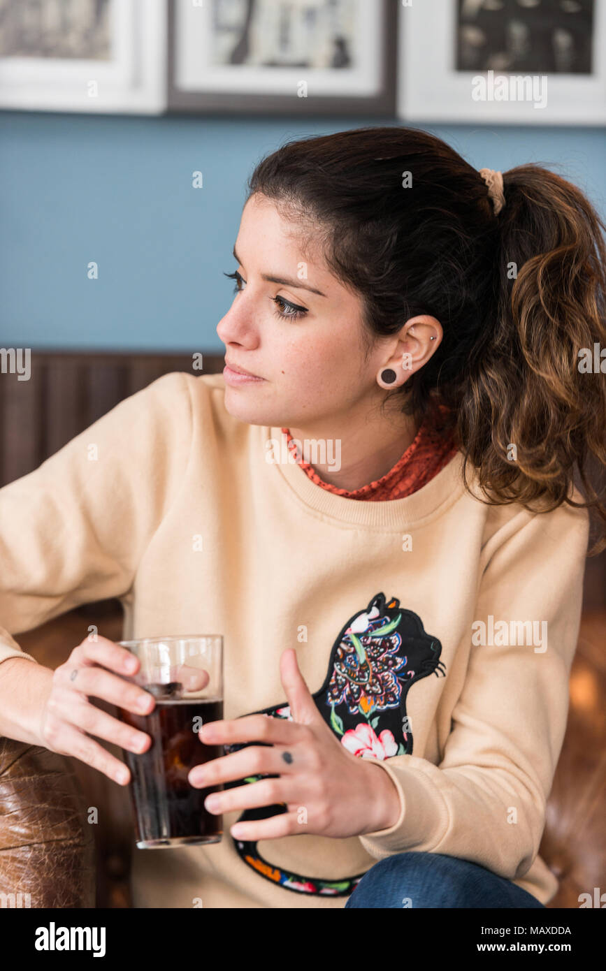 A young brunette woman has a drink sitting on a brown leather sofa in a bar  while using her mobile phone from Cáceres, Extremadura, Spain Stock Photo -  Alamy