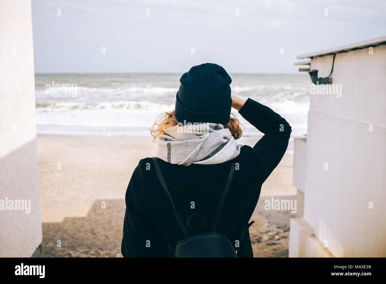 Hipster girl looking at the cold ocean. Rear view of a young woman standing  on the seashore wearing a coat, scarf, hat and backpack. Traveler enjoys t  Stock Photo - Alamy