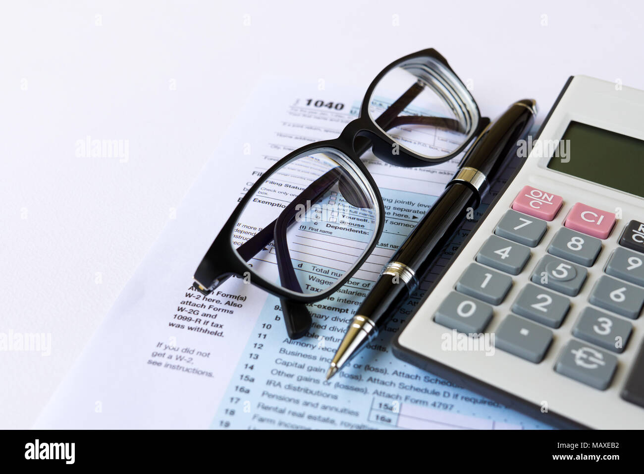 Tax filing - Top view of calculator, pen, eyeglasses and out of focus U.S IRS 1040 form Stock Photo