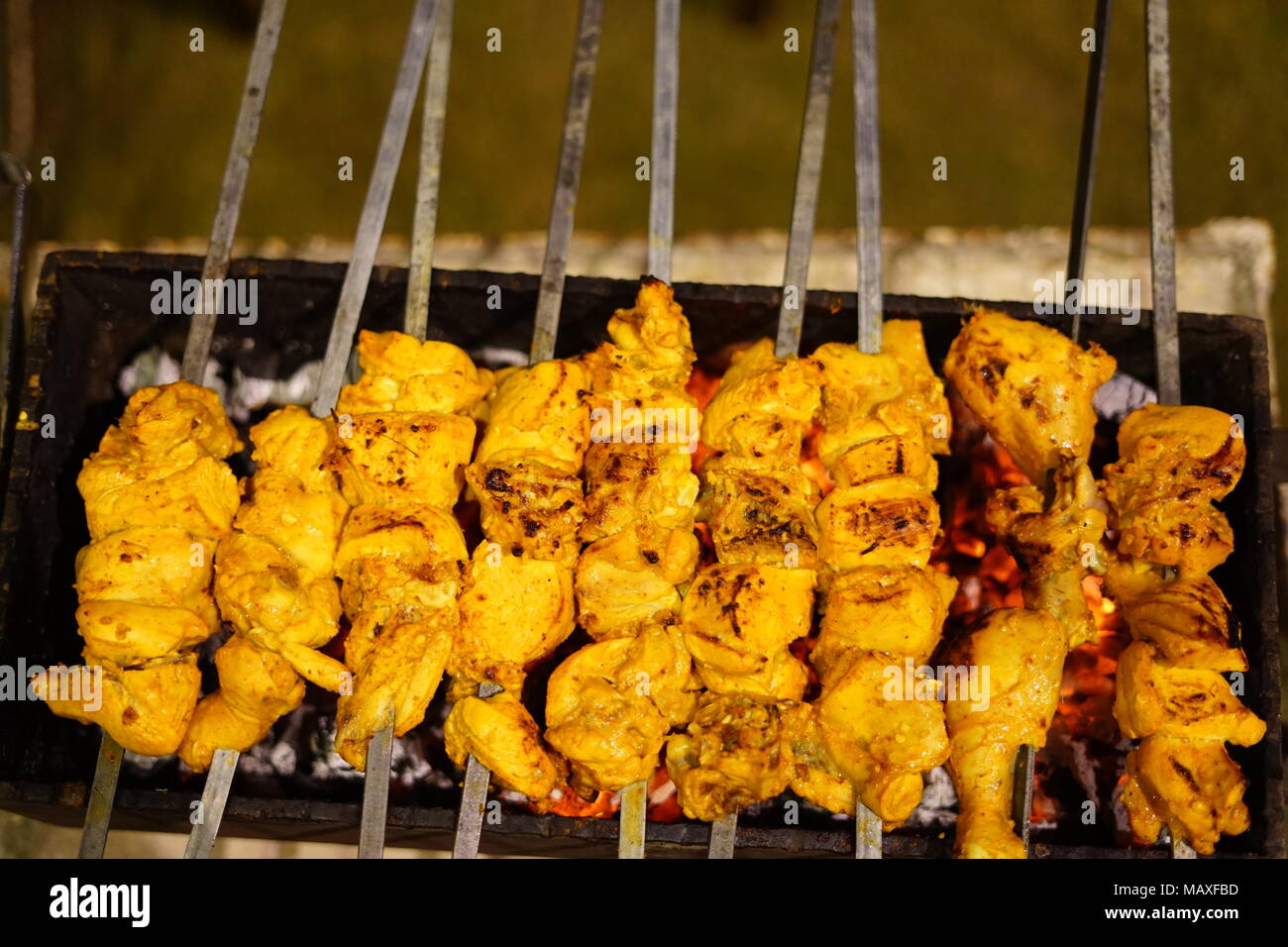 Barbecuing chicken tikka out in the open on traditional stand Stock Photo