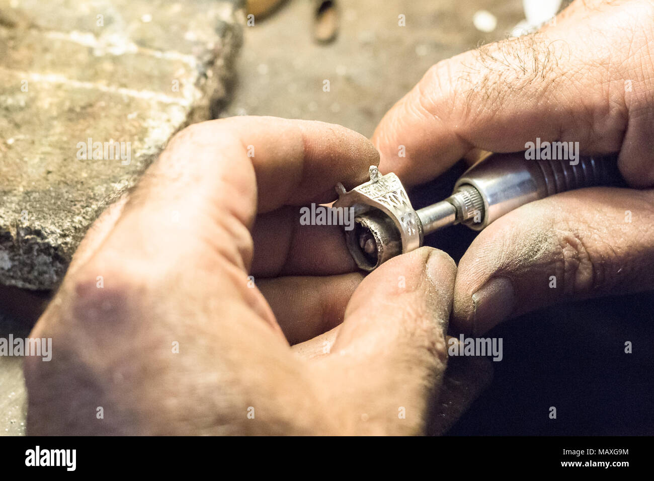 Male jeweler polishing a silver ring with a slotted mandrel for sandpaper, mounted on a flex shaft. Stock Photo