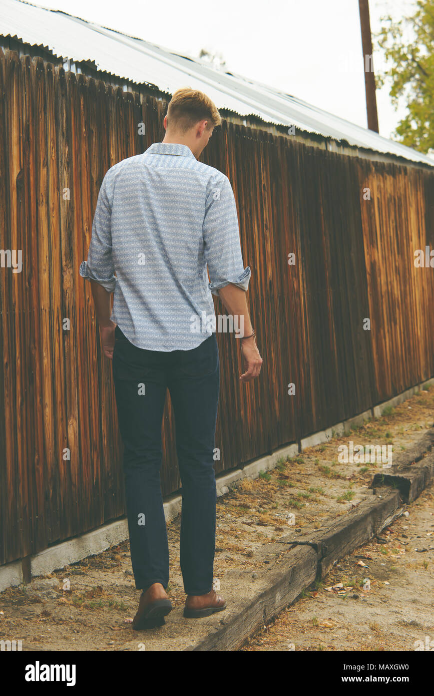 A Caucasian man, slim, short hair, looking down, walking away, back facing camera. An outdoor lifestyle full length portrait concept. Stock Photo