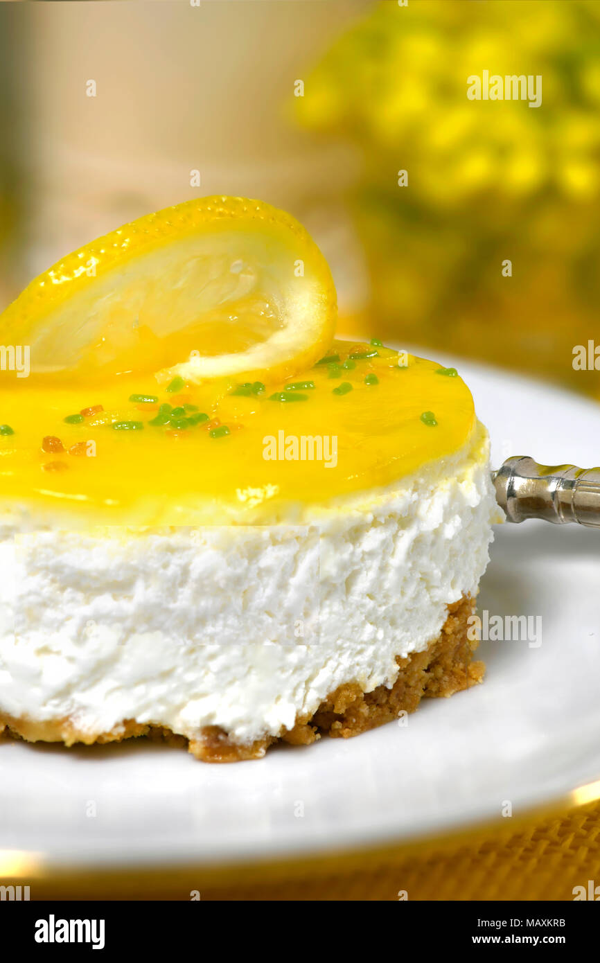 luxury restaurant setting of a lemon mousse cheesecake a silver fork on a white plate soft background with yellow flowers and to ad copy space Stock Photo