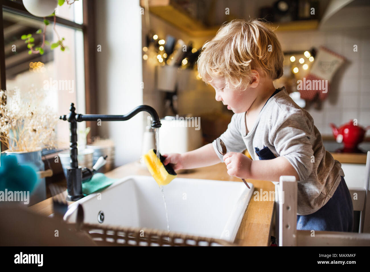 A toddler boy washing up the dishes. Stock Photo