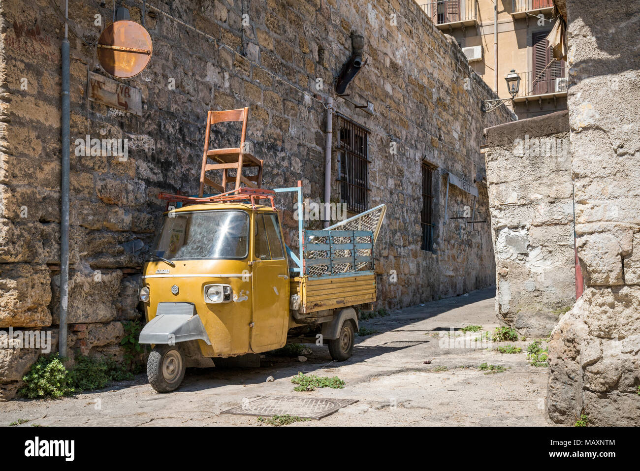 An old yellow Piaggio Ape in the back streets of Palermo in Sicily. Extra seating on top! Stock Photo