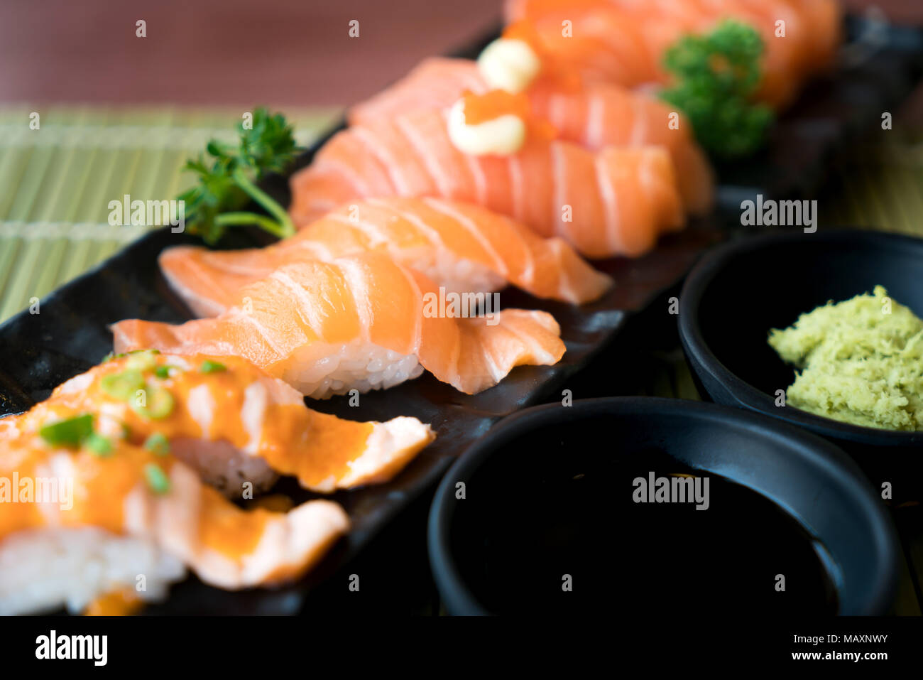 Mixed salmon sushi on black plate along with Japanese sauce and green leaf decoration, Japanese food, close up at sushi . Stock Photo