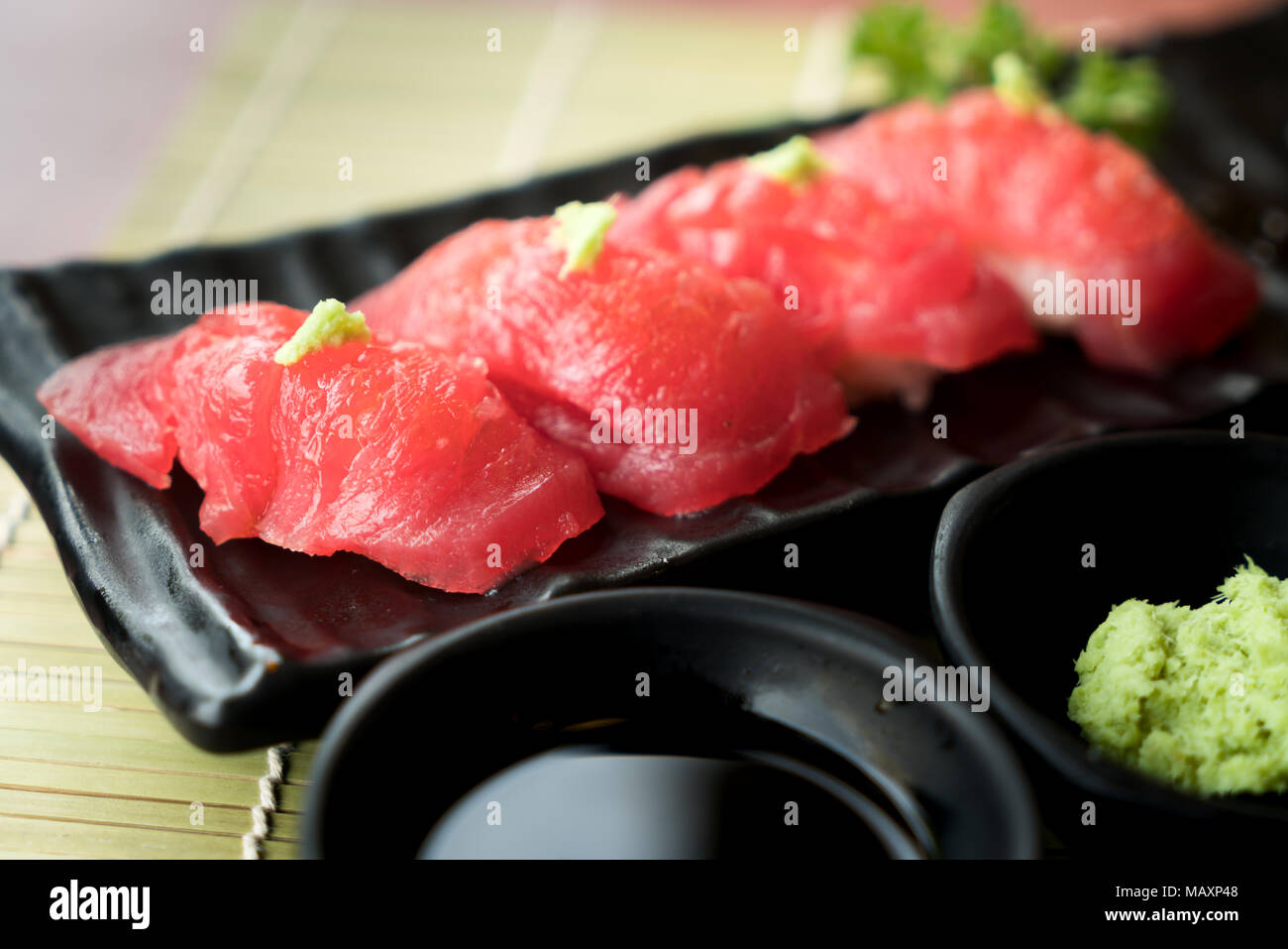 Tuna sushi on black plate along with Japanese sauce and green leaf decoration, Japanese food, close up at sushi . Stock Photo