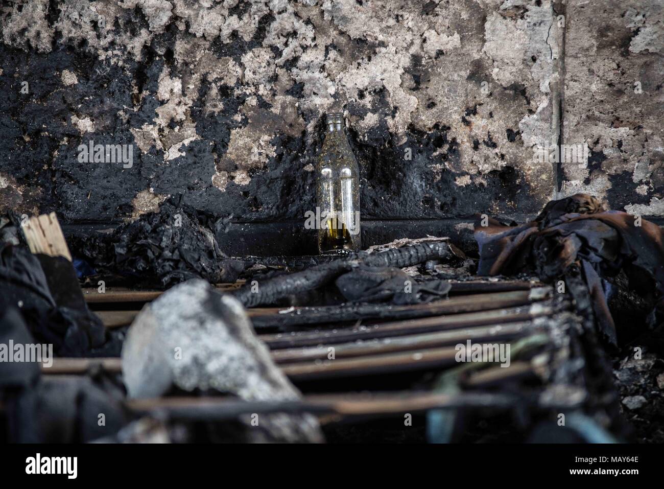 April 5, 2018 - MÃ¼Nchen, Bayern, Germany - A glass bottle stands against the backdrop of the charred wall of a bridge that housed a homeless camp in Munich, Germany. A homeless camp under the ReichenbachbrÃ¼cke (Reichenbach Bridge) in Munich was the target of a suspected arson attack. The photos display the aftermath and the blackening of the surfaces of the bridge, as well as intense heat melting mattresses down to their springs. Damage to the bridge is estimated at 25,000 Euros. Four men, ages 24-53 were living there and unharmed. The suspects may have been two men who were standing nea Stock Photo