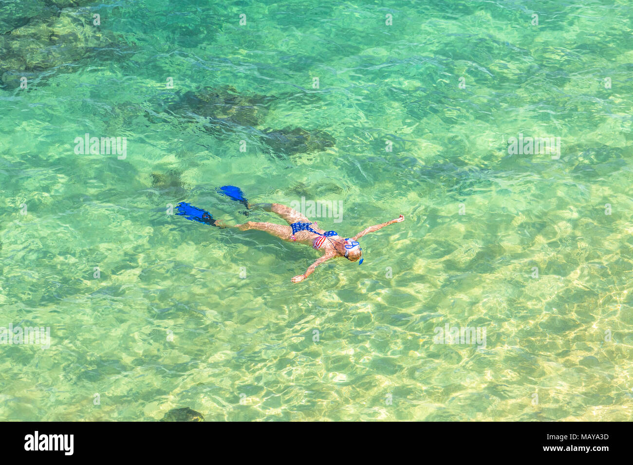 Woman snorkeling over coral reef in Hanauma Bay Nature Preserve, Oahu, Hawaii, USA. Female lying above the crystalline water in tropical sea with american flag bikini. Watersport activity in Hawaii. Stock Photo