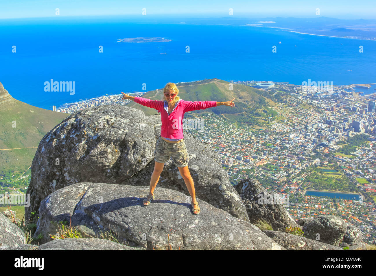 Young woman enjoying panoramic views of Cape Town from the top of Table Mountain National Park in Western Cape, South Africa. Happy female tourist with Port of Cape Town and Waterfront on background. Stock Photo