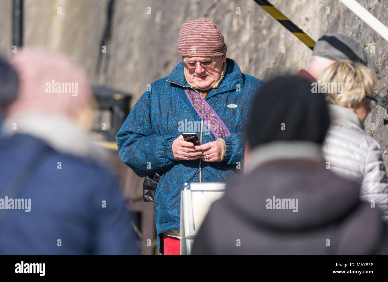 Middle aged or elderly man standing outside texting on a mobile phone in the UK. Senior using technology, sending text. Stock Photo