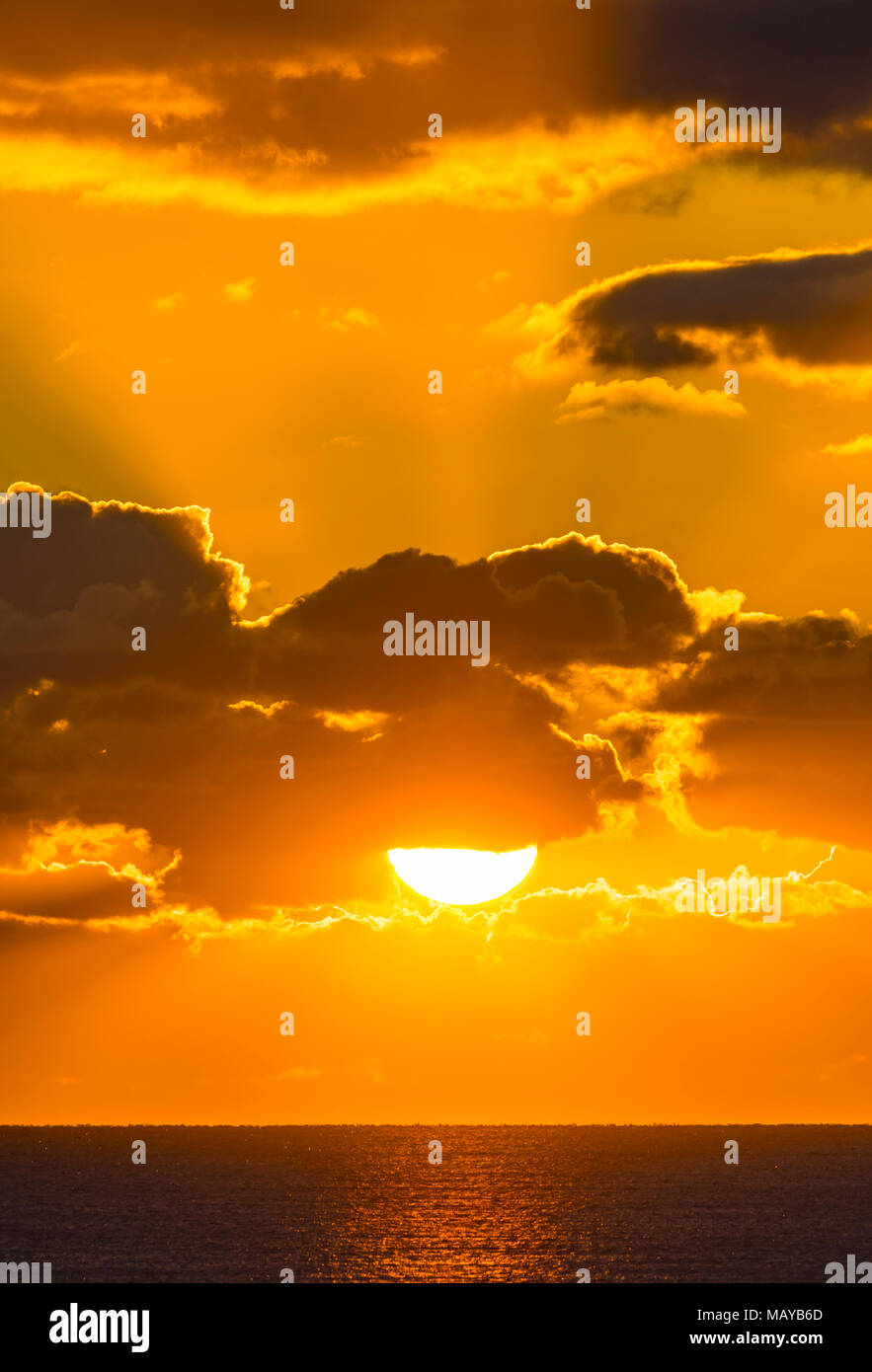 Sunset over the sea with rays from the sun shining through clouds as the cloud partially covers the low sun. Stock Photo