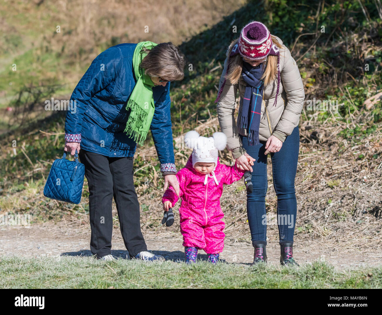 Baby holding hands with 2 women while walking. Possibly first steps or learning to walk. Stock Photo