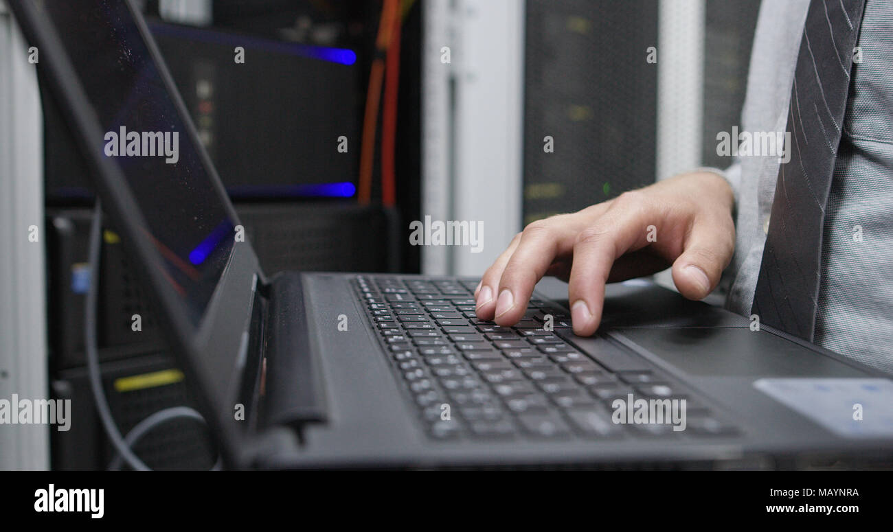 IT data specialist working on laptop on maintaining server rack Stock Photo