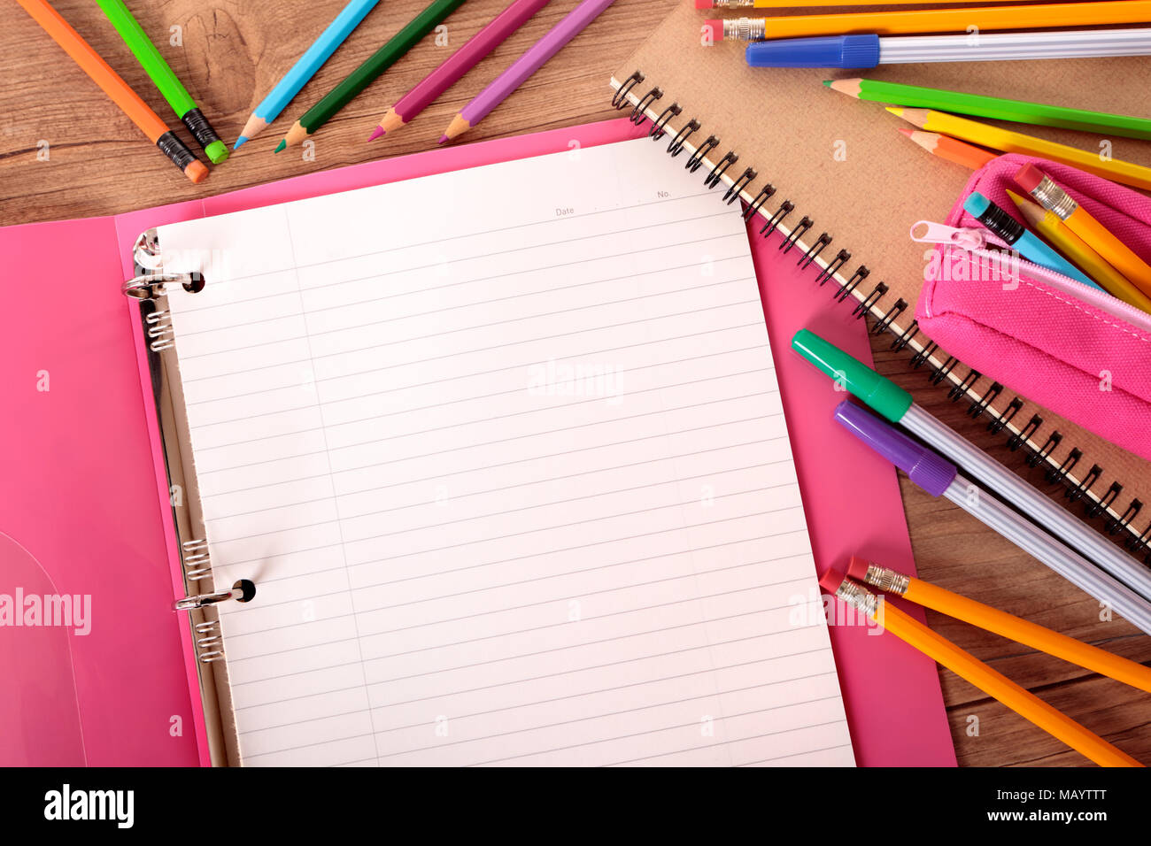 Busy student's desk with pink project folder surrounded by pens, pencils and notebooks. Stock Photo